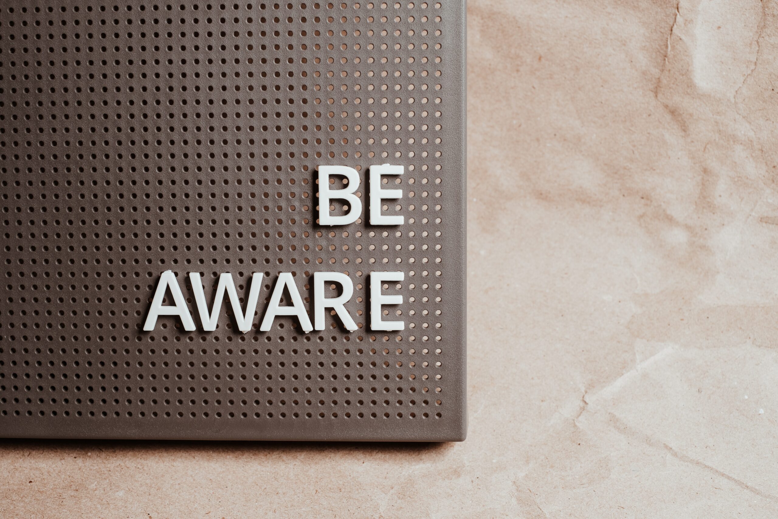 A brownish section of peg-board is shown to be covering about 50% of the picture, positioned mostly in the upper-left portion of the picture. In push-letters on the pegboard, it says "Be Aware".